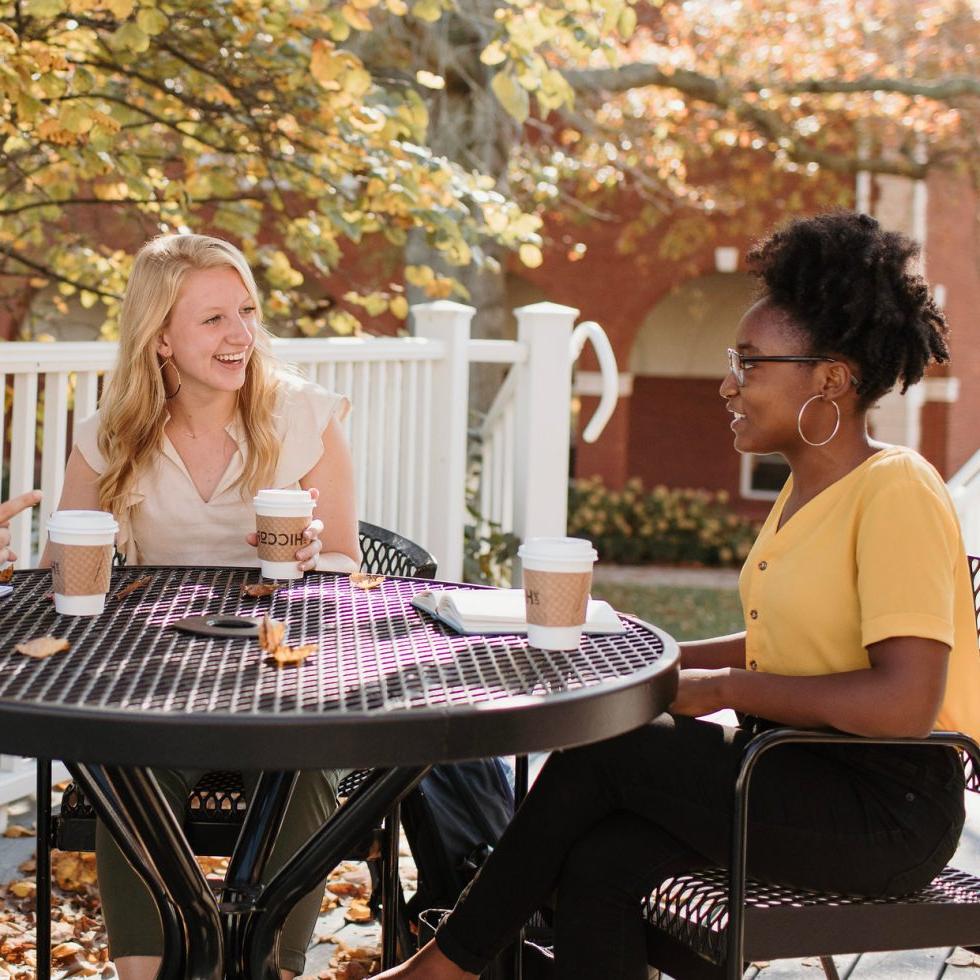 立博体育登录(艾斯拜瑞大学市)校园里的学生们坐在桌子旁愉快地与朋友聊天，桌子上放着咖啡杯.